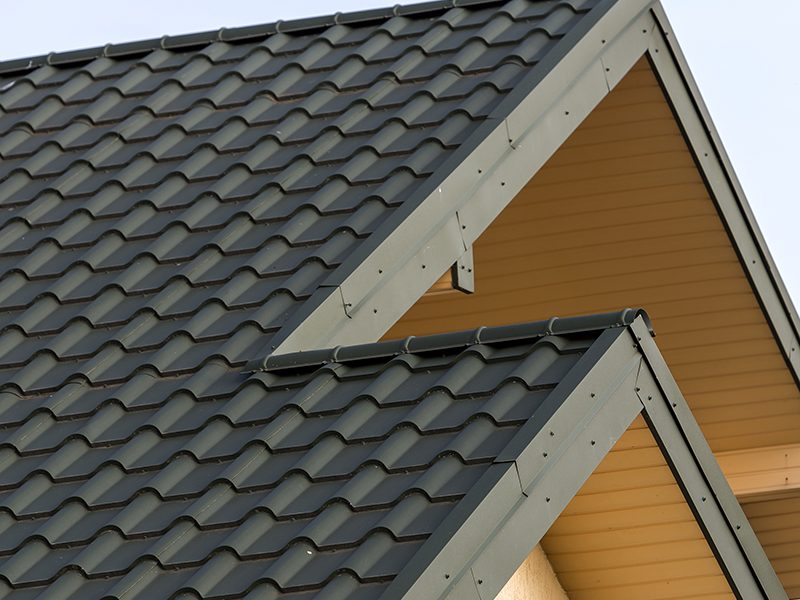 Close-up detail of new modern house top with shingled green roof on clear blue sky background. Professionally done building and construction work, real estate property, contract concept.