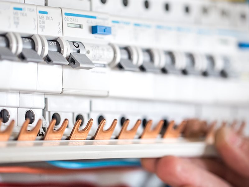 Man, an electrical technician working in a switchboard with fuses. Installation and connection of electrical equipment. Professional with tools in hand. concept of complex work, space for text.