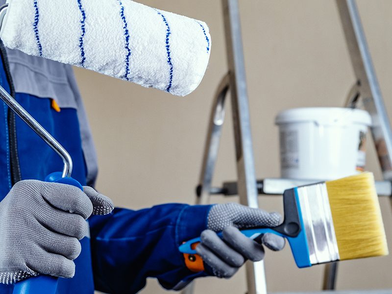 The plaster painter is ready to paint the wall. In the hands of a roller and brush. A stepladder and a bucket of paint in the background